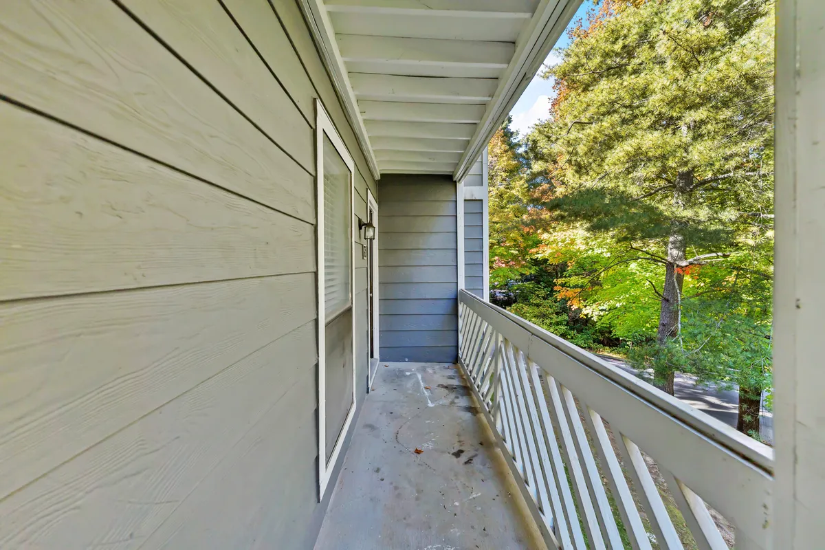 An exterior view featuring a balcony railing overlooking lush surrounding trees, with the building’s exterior wall in sight. The scene suggests a quiet, leafy setting, offering a glimpse into the environment guests can enjoy from the property.