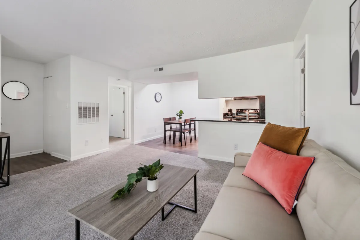 A broad view of the living area shows a sofa with accent pillows, a coffee table with a plant, and a dining area in the background. The room radiates coziness and is clearly set up for both relaxing and socializing, reflecting a move-in-ready atmosphere.