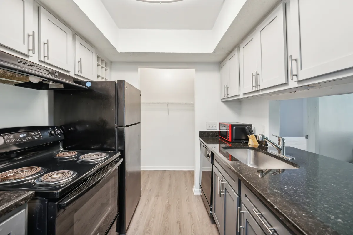 A contemporary kitchen scene featuring black appliances, expansive granite countertops, and bright white cabinets. The space is bustling with activity, suggesting meal preparation and social interaction. The inviting setup hints at both functionality and a welcoming atmosphere for guests or family gatherings.